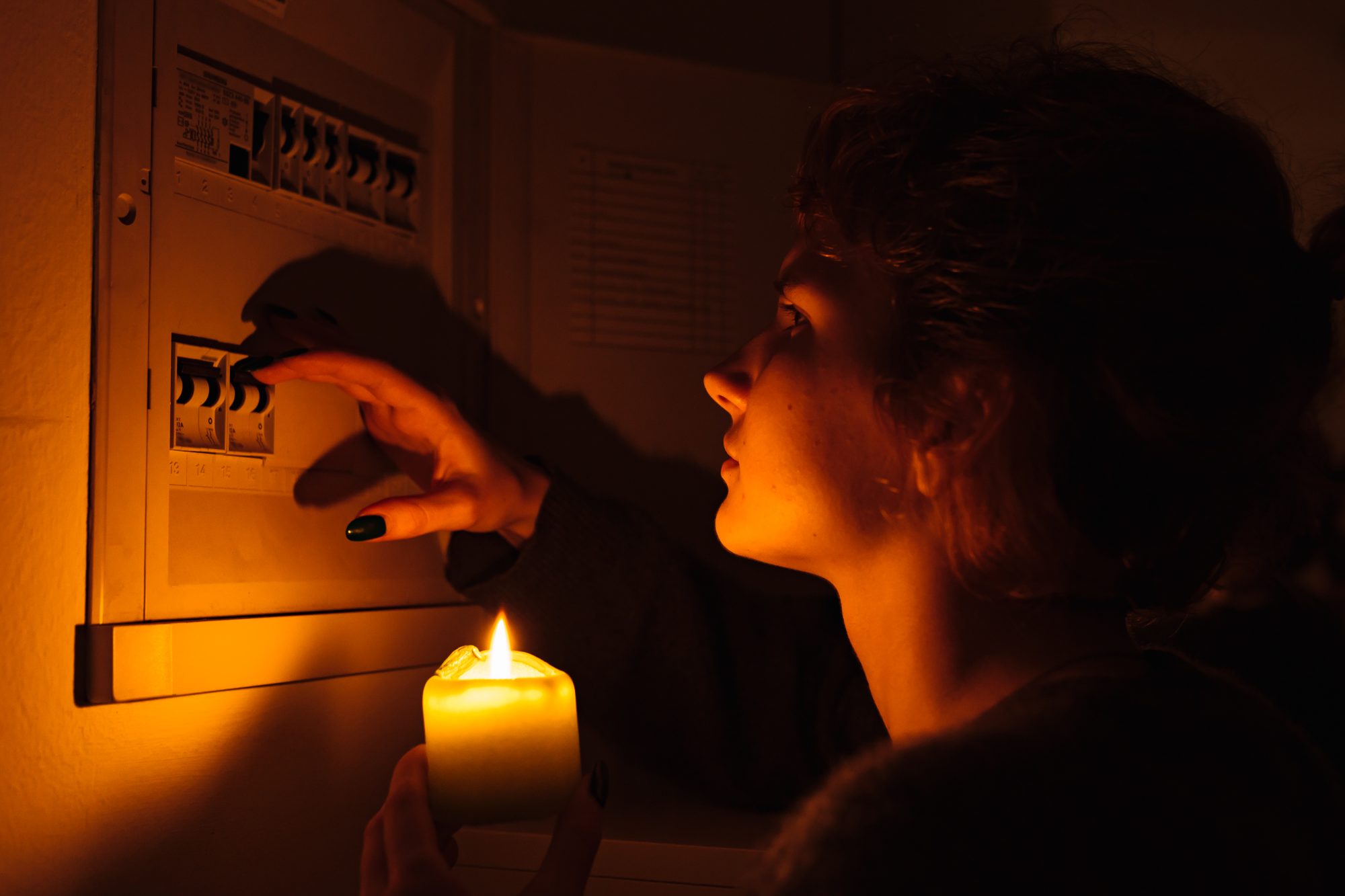 Pessoa ligando o interruptor de luz enquanto segura uma vela.